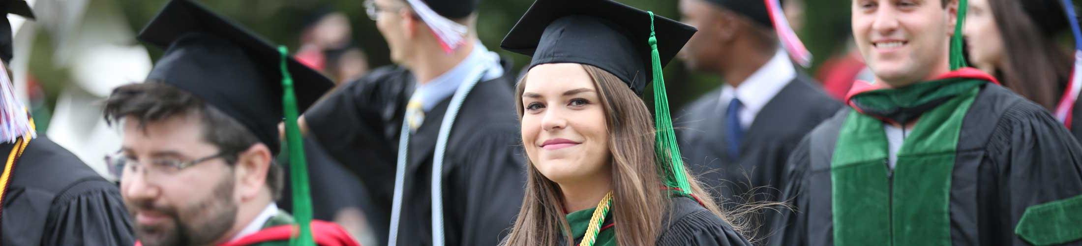 Graduate smiling at camera outside walking to commencement